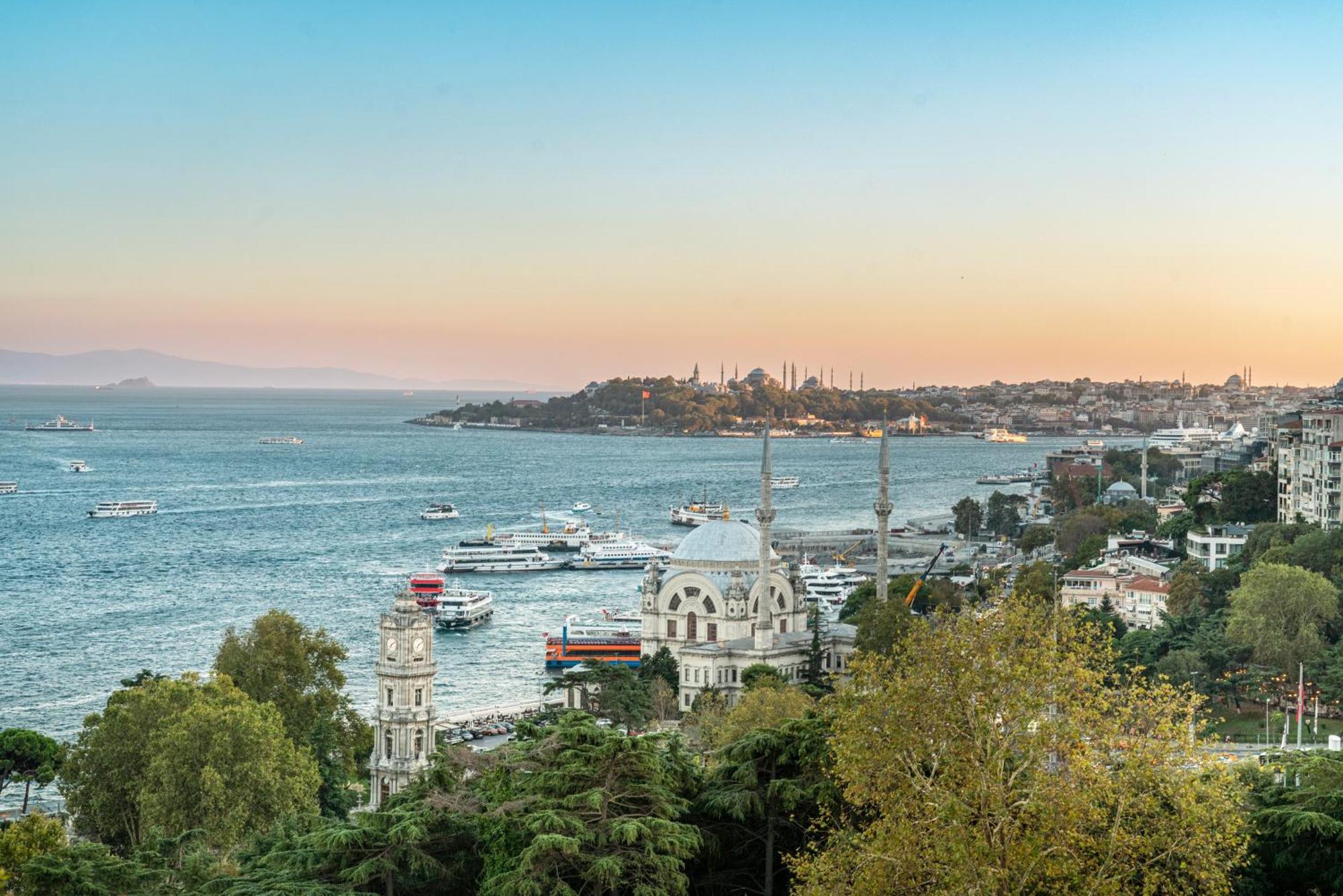 Swissotel The Bosphorus Istanbul Exterior photo The photo shows a picturesque view of a coastal area during the evening, with a serene body of water. In the foreground, there are several trees and buildings, including distinctive architectural structures, likely mosques or historical sites, with m