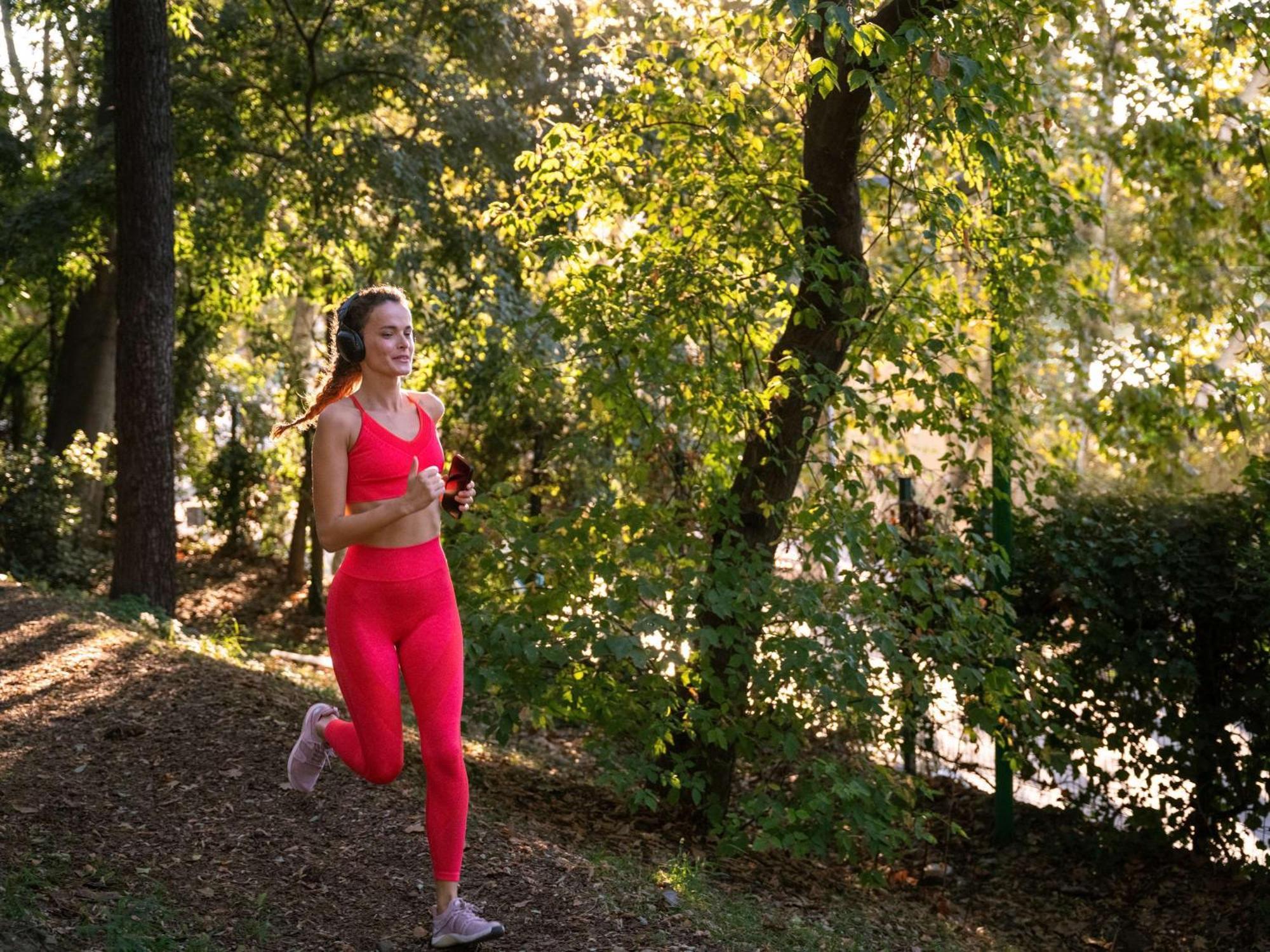 Swissotel The Bosphorus Istanbul Exterior photo The photo shows a woman jogging along a path in a natural setting. She is wearing bright pink athletic attire, including a tank top and leggings. The background features trees with green leaves, indicating it's a sunny day. The sunlight filters throu