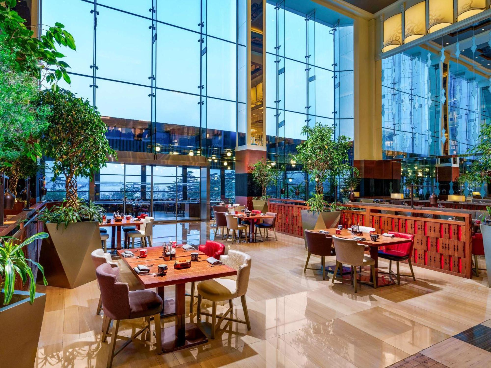 Swissotel The Bosphorus Istanbul Exterior photo The photo shows a modern restaurant interior featuring large glass windows that allow plenty of natural light to enter. The decor includes lush greenery, with potted plants placed throughout the space. There are several dining tables arranged comfort