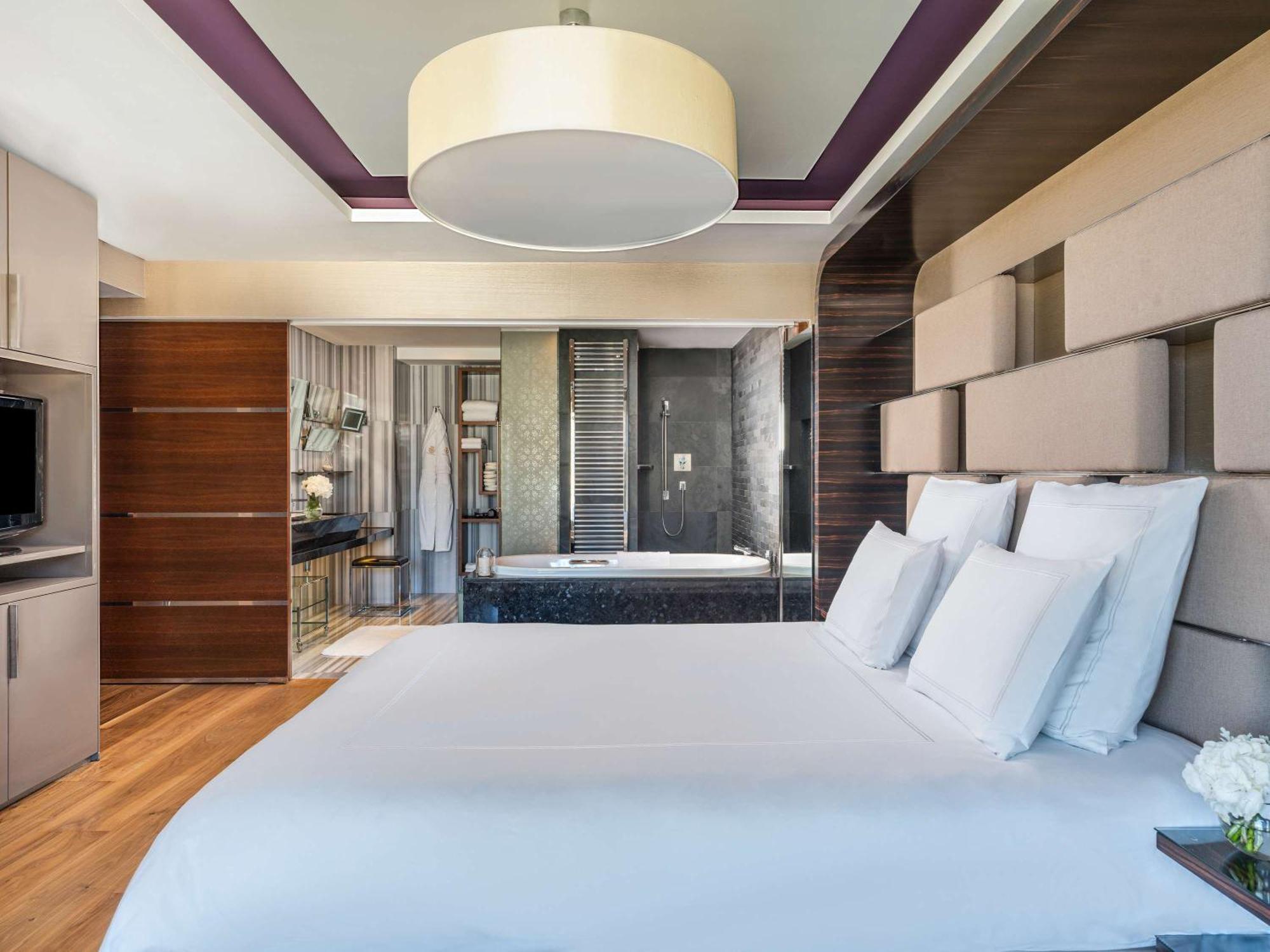 Swissotel The Bosphorus Istanbul Exterior photo The photo shows a modern hotel room featuring a large bed with white bedding and multiple white pillows. The room has a stylish, contemporary design, with a curved ceiling light fixture above the bed. On one side, there's a flat-screen television mou