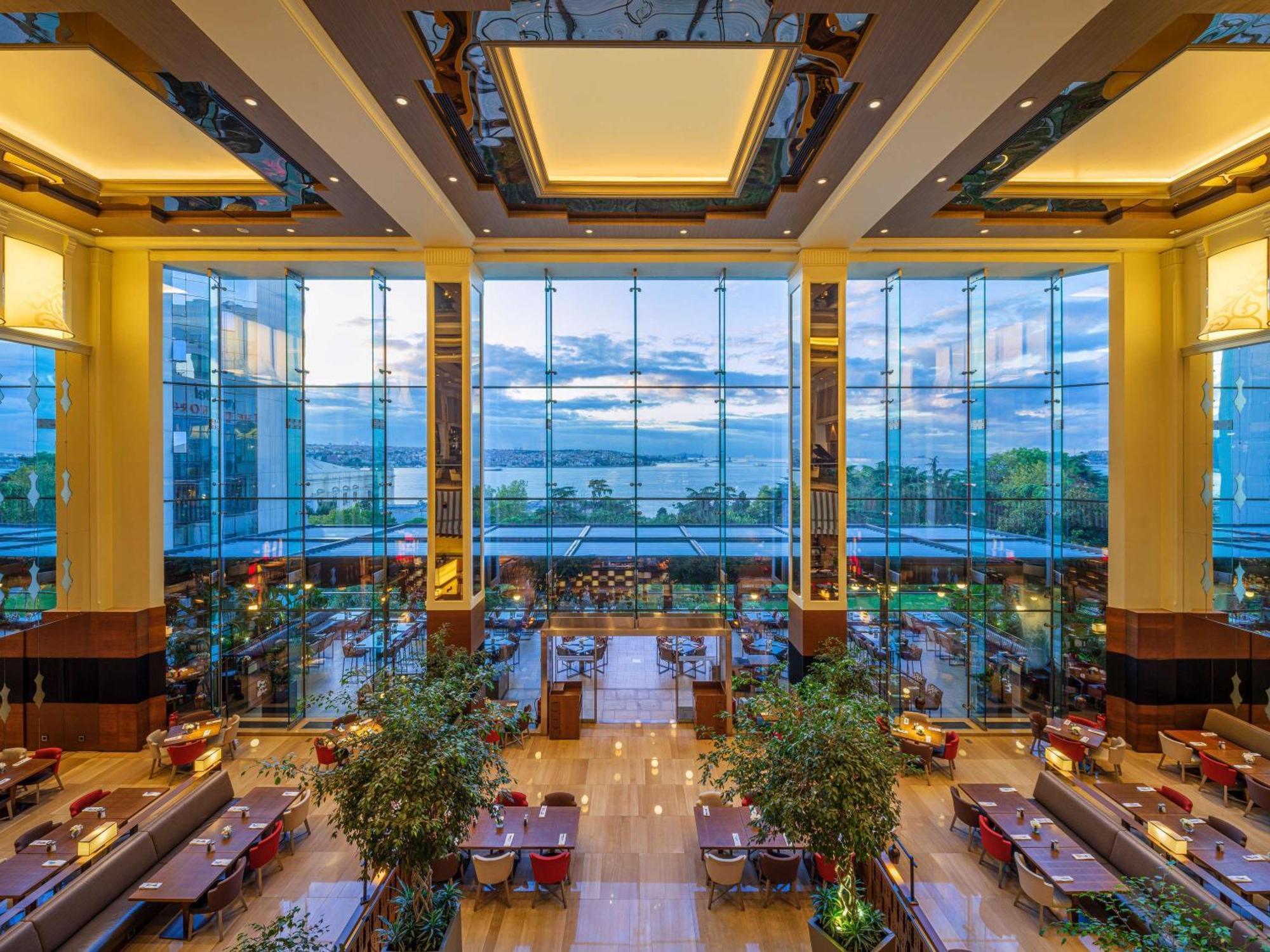 Swissotel The Bosphorus Istanbul Exterior photo The photo shows the interior of a modern restaurant with a spacious and elegant design. Large glass windows allow plenty of natural light to flood the space, offering a view of the outdoors, which appears to include a scenic landscape. The decor feat